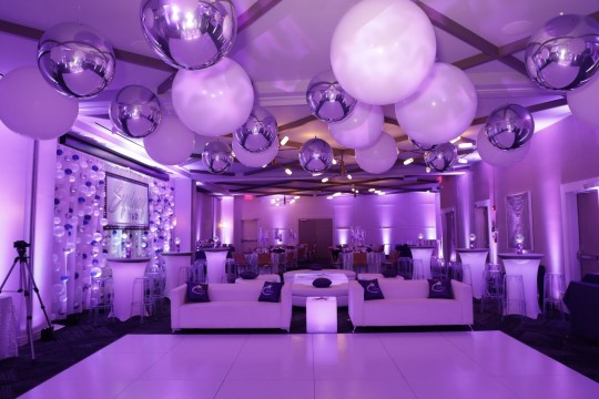 Beautiful LED Lounge Setup for Kids VIP Seating, with Custom Logo Pillows, High Tops, Purple Uplighting Around the Room, Classic Ceiling Treatment with Large Balloons and Orbz, Custom Backdrop and Bubble Balloon Wall